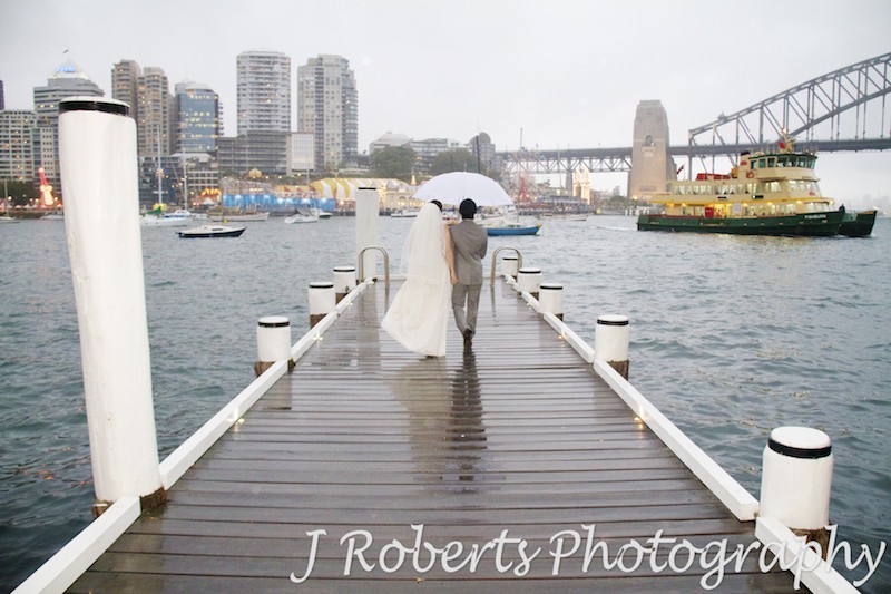 Bride and groom walking along a jetty in the rain on Sydney Harbour - wedding photography sydney